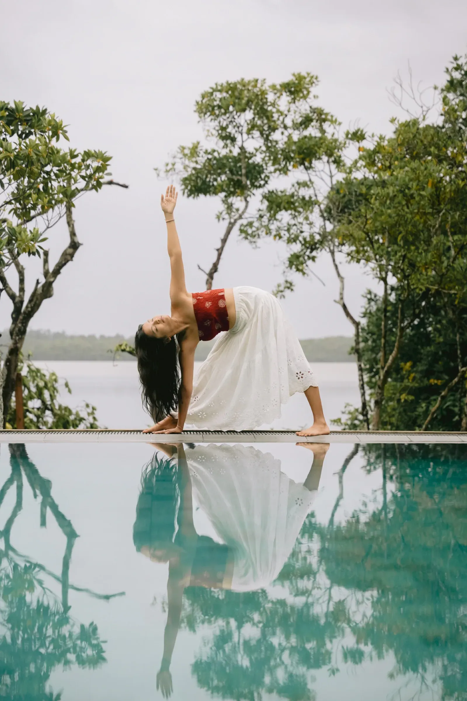 Ein Gast in einer Yogahaltung am Poolrand, im Wasser gespiegelt, dahinter der Koggala-See