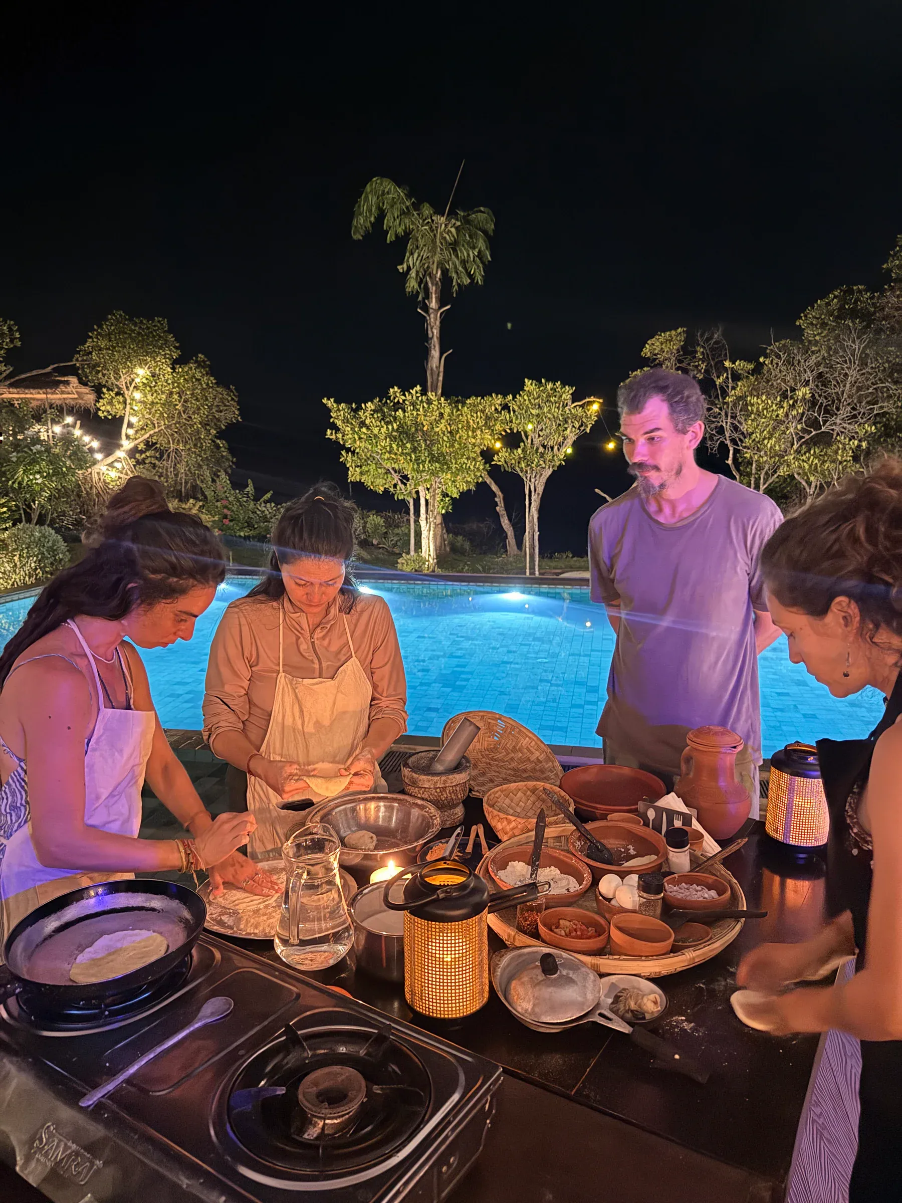 Gäste bei einem abendlichen Kochkurs am beleuchteten Pool