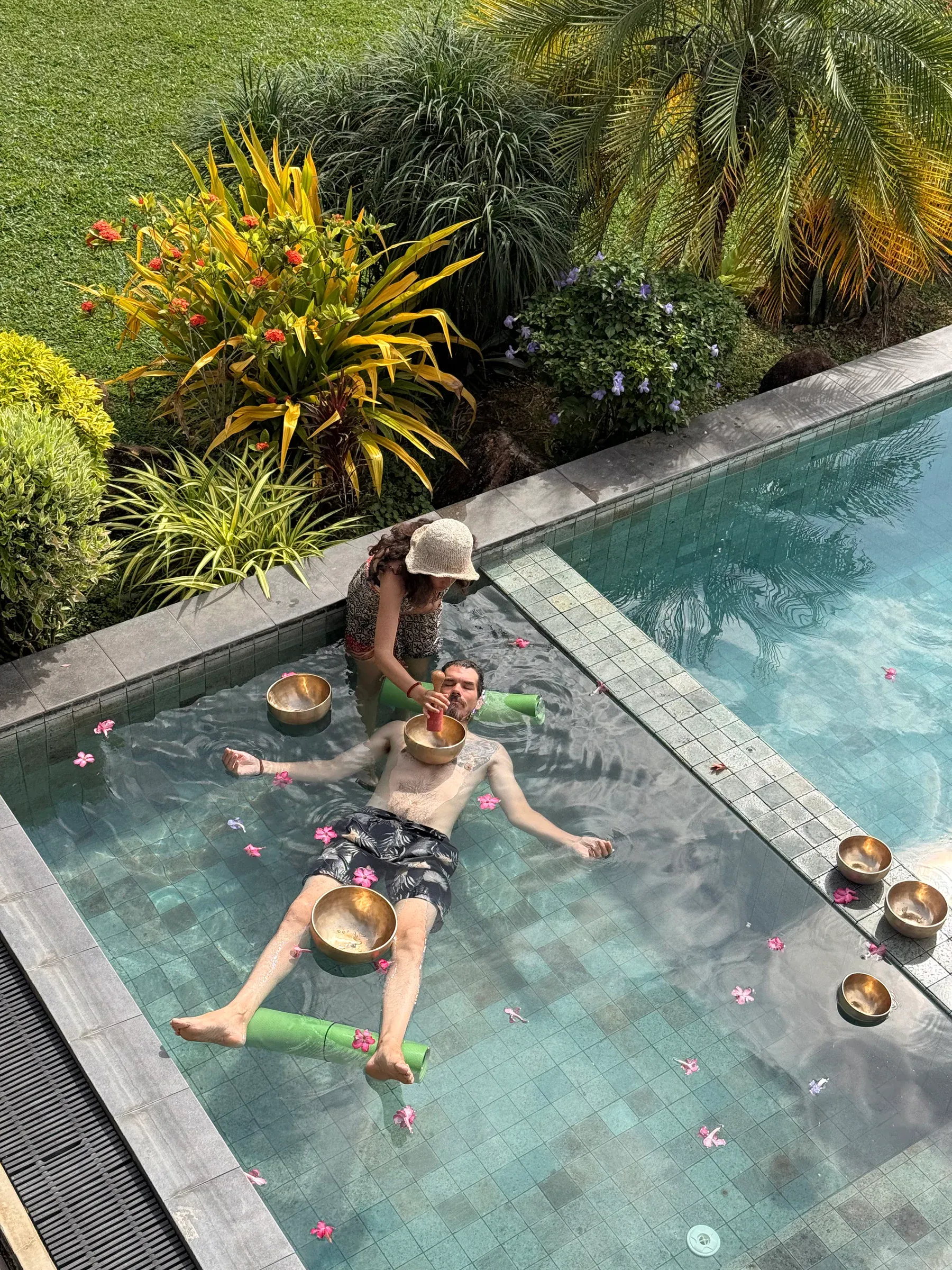 Von oben: Ein Gast treibt im flachen Teil des Pools zwischen Klangschalen und Blütenblättern