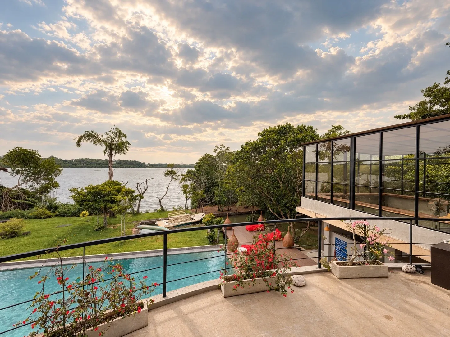 Von einer oberen Terrasse: unten der geschwungene Pool, dahinter die Wiese und der Koggala-See unter einem Abendhimmel