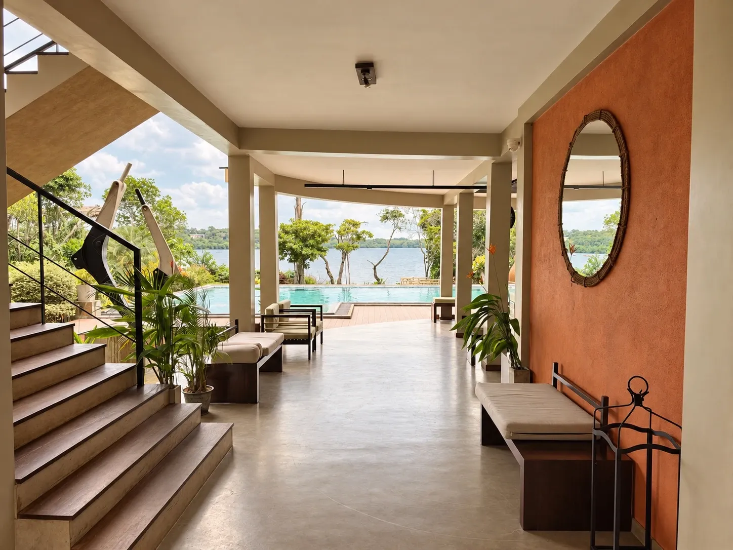 Die offene Lounge: ein Gang an einer orangefarbenen Wand mit rundem Spiegel vorbei, hinaus zum Pool und zum See