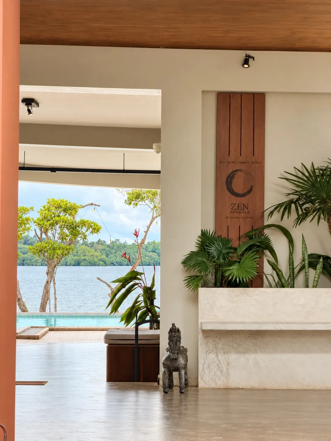 Eine Holzwand mit dem Zen-Ensō neben Pflanzen und ein Durchblick zum Pool und zum See