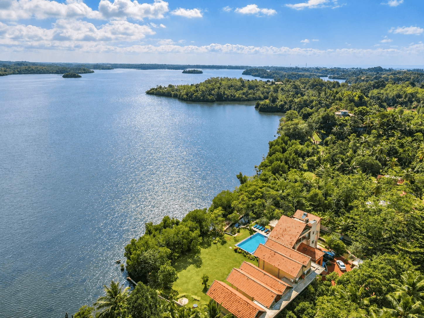 Luftaufnahme, farblich bearbeitet: der Koggala-See mit seinen bewaldeten Inseln, unten rechts am Ufer die Terrakottadächer der Villa, der Pool und die Wiese